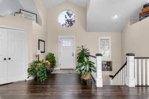 Vaulted ceiling entry featuring dark wood-finish flooring, a full-lite entry door, a circular accent window, and a white and black staircase