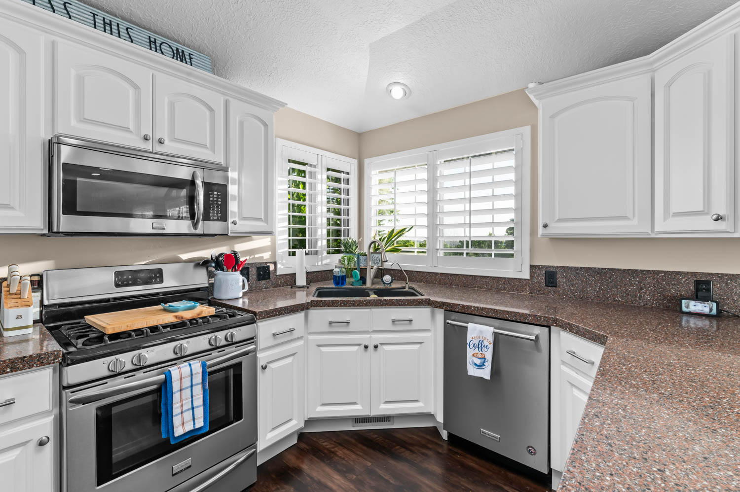 Kitchen featuring white cabinetry, stainless steel appliances, dark stone-finish countertops, wood-finish flooring, and white plantation shutters