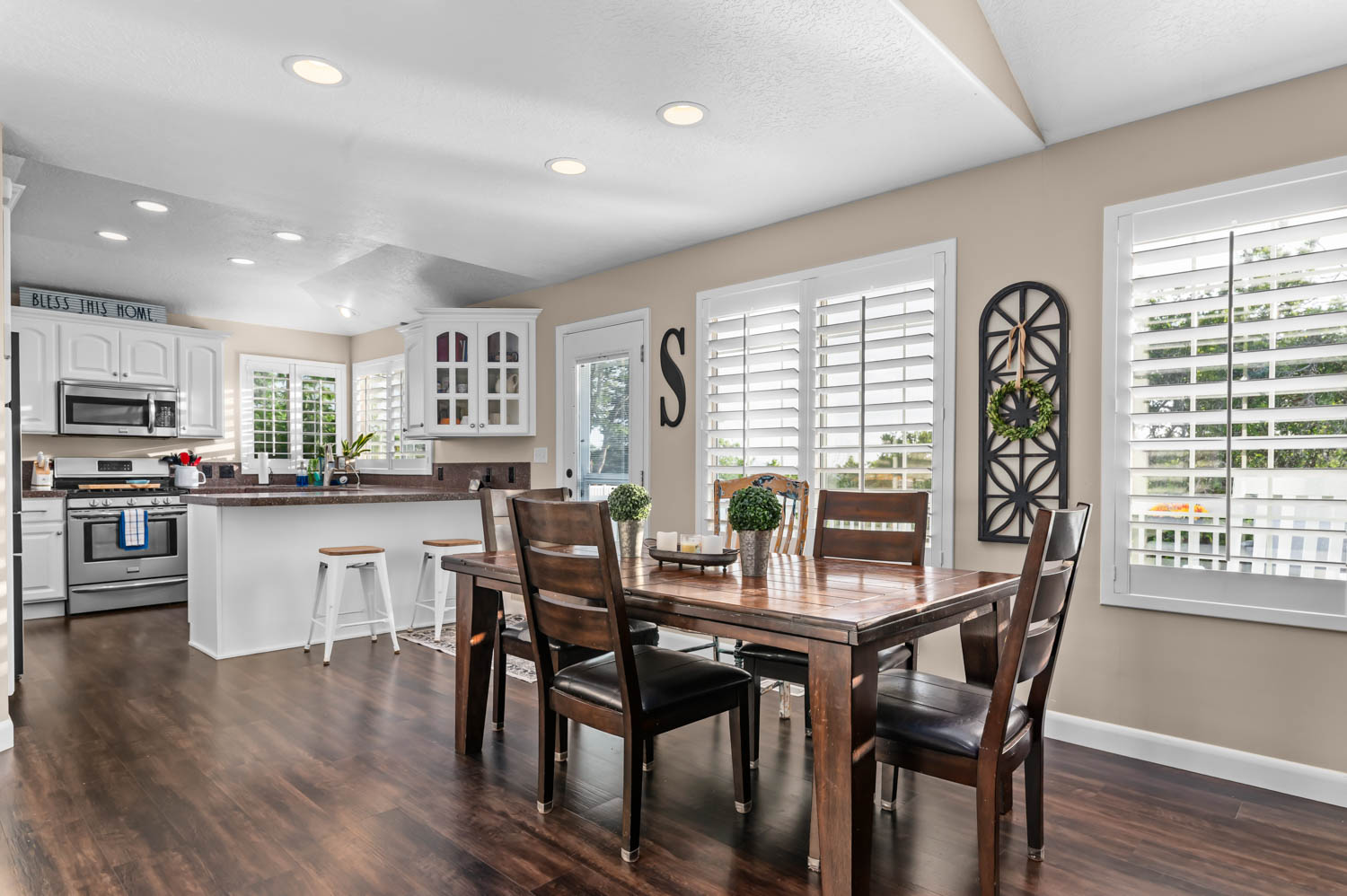 Open-concept kitchen and dining area featuring rich wood-finish flooring, white cabinetry, stainless steel appliances, and recessed lighting