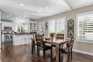 Open-concept kitchen and dining area featuring rich wood-finish flooring, white cabinetry, stainless steel appliances, and recessed lighting