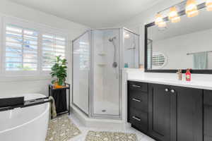 Modern bathroom featuring a standalone corner shower with glass enclosure, a freestanding soaking tub, dual windows with plantation shutters, a dark wood-finish vanity with a white countertop, and a large wall-mounted mirror with an overhead light fixture
