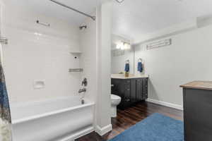 Bathroom featuring a white subway tile tub surround, dark wood-finish flooring, a single vanity with a dark cabinet, and a wall-mounted mirror with overhead lighting