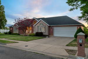 Single-story residence featuring a two-car garage, manicured lawn, and mature trees