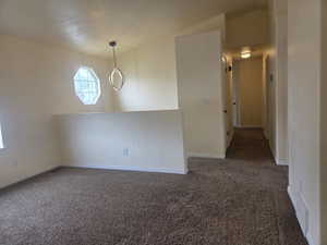 Carpeted interior space featuring a modern chandelier, octagonal window, vaulted ceiling, and a hallway with a flush-mount light fixture
