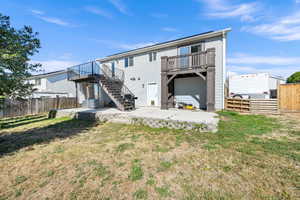 Two-story property featuring light gray siding, a concrete patio, a wooden fence, and a multi-level deck with black railings and stairs