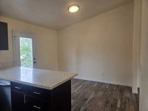 Kitchen area featuring a white quartz countertop island with dark wood cabinetry and chrome hardware, wood-finish flooring, and a glass-paneled door leading to an exterior balcony with a black railing