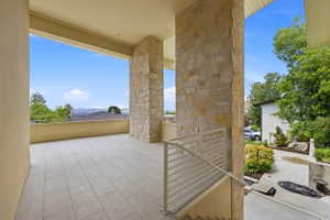 Expansive outdoor patio featuring light-toned large format tile flooring, stone-clad architectural columns, a beige painted railing, and an elevated position