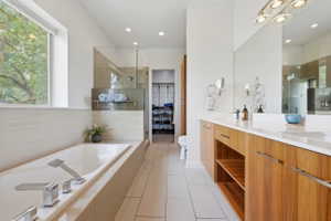Spacious bathroom featuring a built-in soaking tub with chrome fixtures, a walk-in shower with glass enclosure, a double vanity with wood-finish cabinetry, and white countertops
