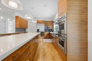 Gourmet kitchen with extensive wood-finish cabinetry, a large central island featuring a white countertop, and stainless steel appliances including a built-in double oven and refrigerator