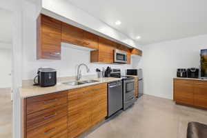 Contemporary kitchen featuring wood-finish cabinetry, light-toned countertops, and stainless steel appliances including a microwave, range, and dishwasher