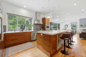 Kitchen featuring a large central island with seating, a stainless steel range hood, built-in oven, and wood-finish cabinetry