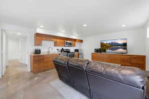 Open concept living space featuring a full kitchen with stainless steel appliances, wood-finish cabinetry, and solid surface countertops