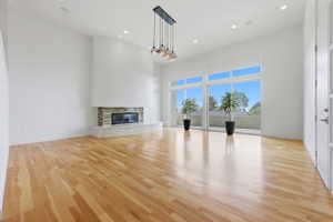 Spacious living area featuring light wood-finish flooring, a stone-clad fireplace, and expansive floor-to-ceiling windows