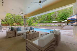 Expansive covered patio featuring a large swimming pool, integrated outdoor kitchen area, two ceiling fans, and a stone accent wall
