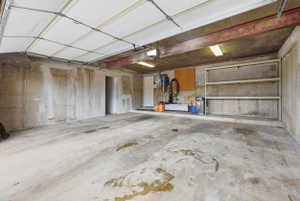 Attached garage featuring a concrete floor, exposed structural beams, and overhead lighting