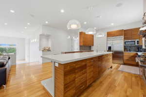 Open-concept kitchen with wood-finish cabinetry, stainless steel appliances, a large center island with a light-toned countertop, and recessed lighting
