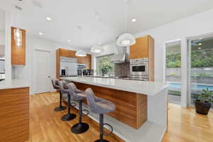Contemporary kitchen featuring a large center island with a white countertop, wood-finish cabinetry, stainless steel appliances, and a mosaic tile backsplash