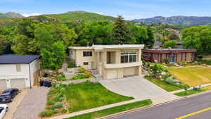 Contemporary architecture featuring a stucco and stone exterior, multi-level landscaping with mature plantings, an integrated two-car garage, and a concrete driveway