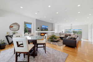 Open-concept living area featuring wood-finish flooring, recessed lighting, a modern fireplace with a tiled surround, and large windows