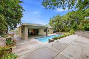 Outdoor concrete patio featuring a rectangular swimming pool, an adjacent covered patio area, and integrated planters