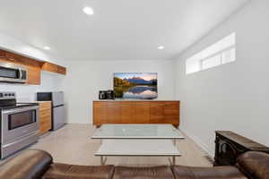 Compact living area featuring an integrated kitchen with stainless steel appliances, wood-finish cabinetry, and a light countertop