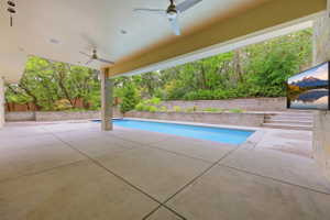 Expansive covered patio featuring a rectangular swimming pool, concrete hardscaping, stone veneer columns, and dual ceiling fans