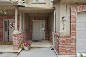 Covered entryway featuring a beige door with a decorative glass insert, complemented by brick detailing and stucco siding