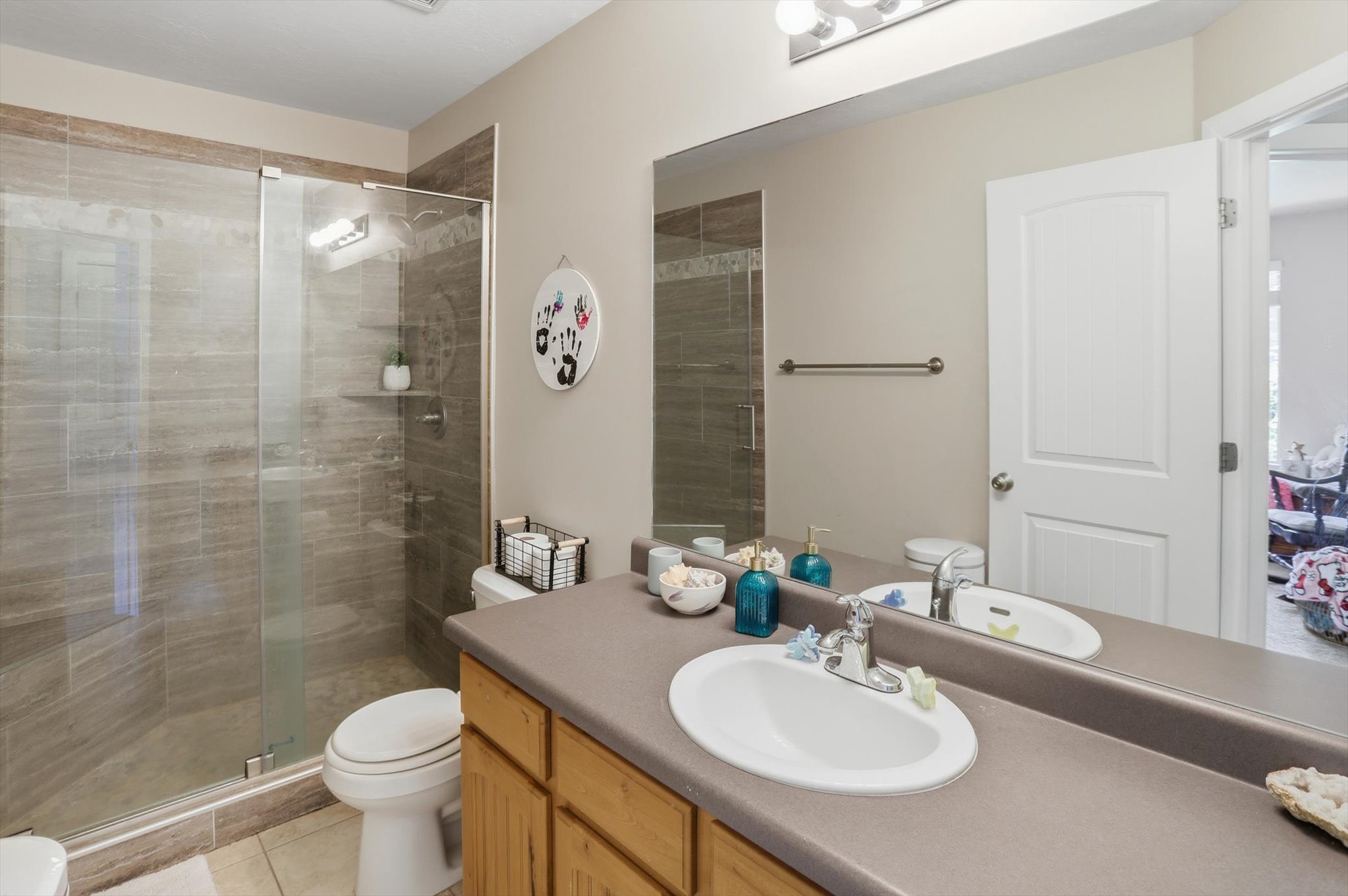 Bathroom featuring a glass-enclosed shower with tile surround, a single vanity with a laminate countertop, a large wall-mounted mirror, and wood-finish cabinetry