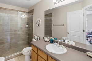Bathroom featuring a glass-enclosed shower with tile surround, a single vanity with a laminate countertop, a large wall-mounted mirror, and wood-finish cabinetry