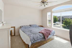 Carpeted room featuring a vaulted ceiling with a ceiling fan, a large arched window, and an additional rectangular window