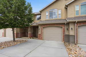 Exterior featuring tan stucco, brick veneer accents, and a shingle roof