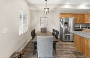 Open-concept dining area featuring wood-finish flooring, a contemporary linear chandelier, and a large window with blinds