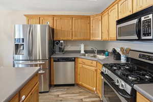 Kitchen featuring light wood cabinetry with beadboard accents, stainless steel appliances, a double-basin sink, and gray countertops