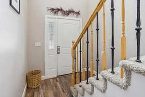 Entryway featuring wood-finish flooring, a white door with decorative glass sidelight, and a staircase with carpeted treads and a natural wood handrail with black metal balusters