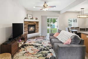 Cozy living space featuring a stone-clad corner fireplace with a white mantel, wood-finish flooring, and a ceiling fan