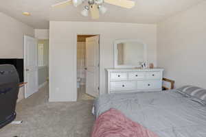 Carpeted bedroom featuring a ceiling fan with light fixture, neutral wall color, and a door opening to a bathroom with tile flooring and a shower curtain