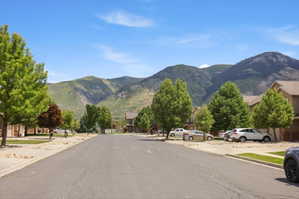 Neighborhood street featuring mature trees, paved sidewalks, and mountain scenery