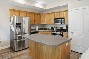 Kitchen featuring wood-finish cabinetry, stainless steel appliances, a center island with a grey countertop, and wood-finish flooring
