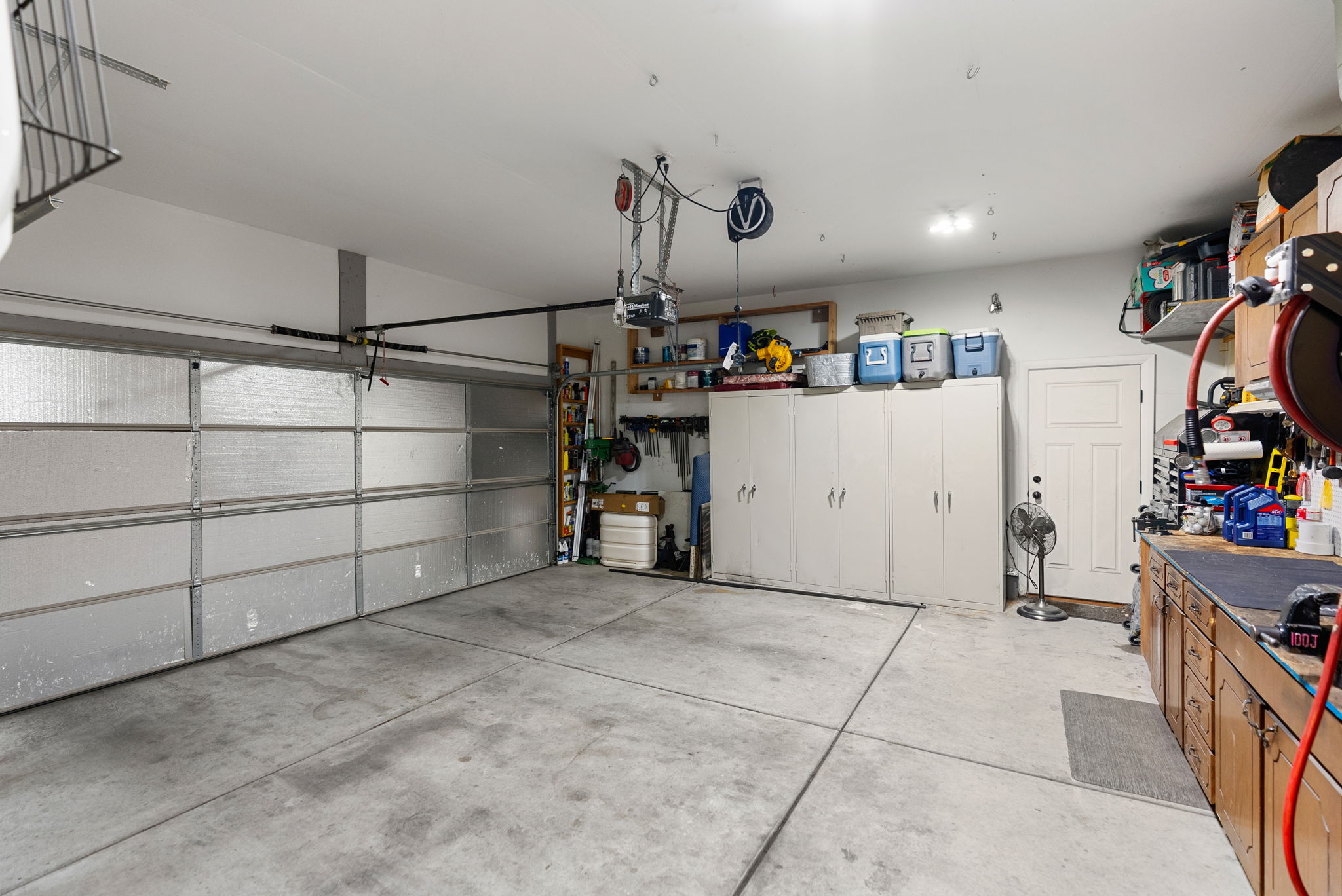 Spacious garage featuring a sectional garage door, concrete flooring, extensive built-in cabinetry, and a work bench with upper shelving