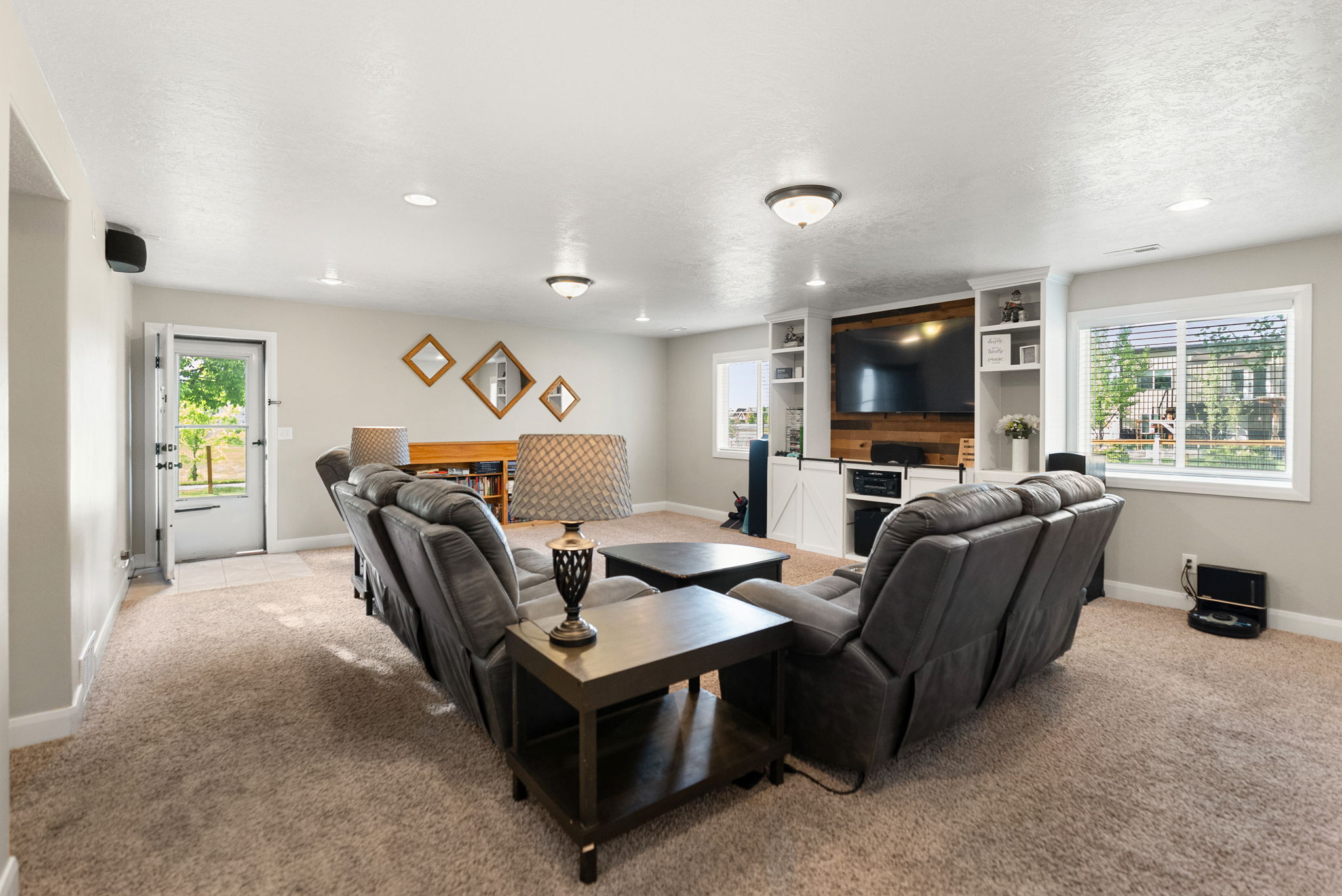 Spacious entertainment area featuring neutral-toned carpeting, recessed lighting, and a built-in media center with shelving