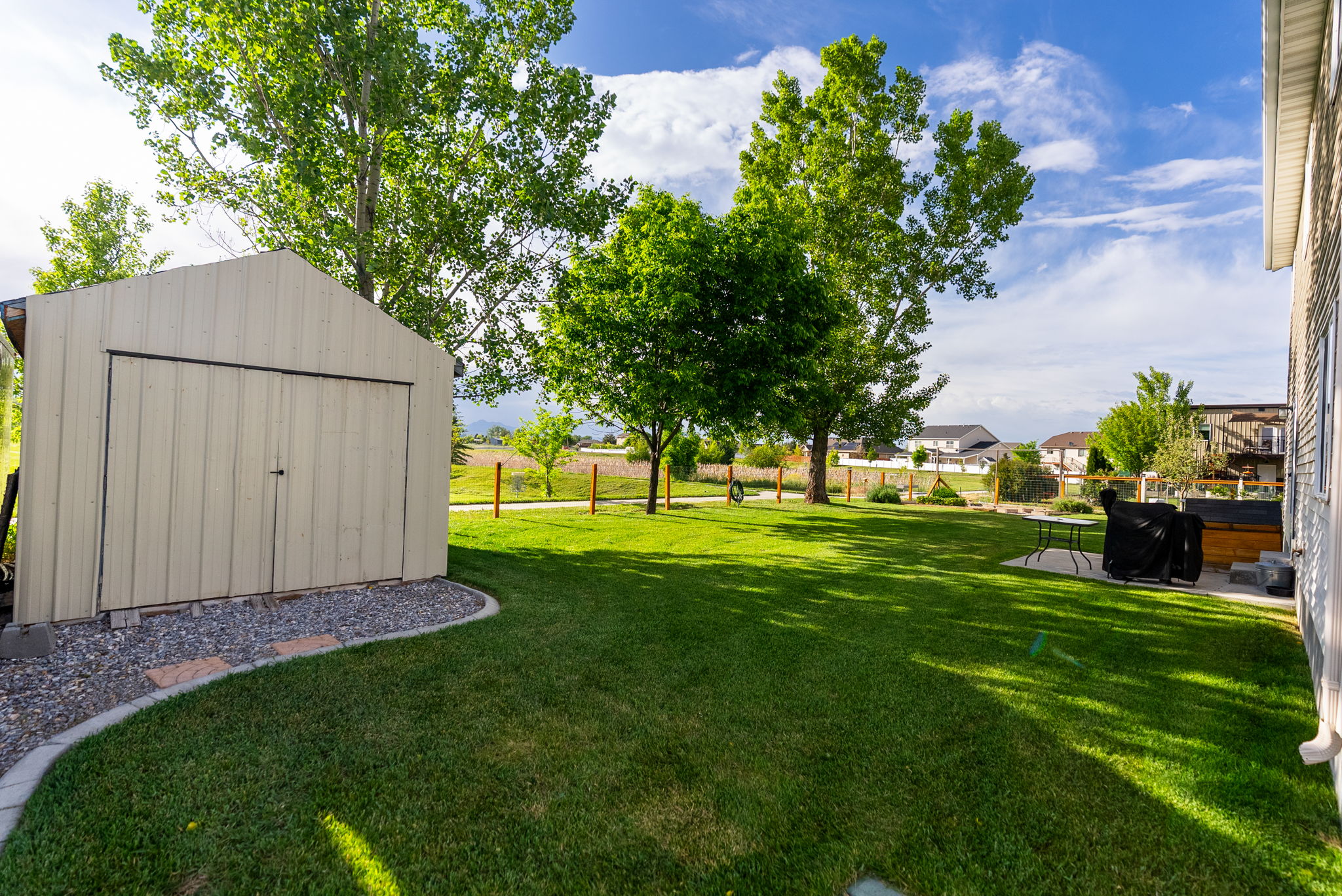 Expansive green lawn featuring a storage shed with double doors, bordered by a gravel and paver pathway