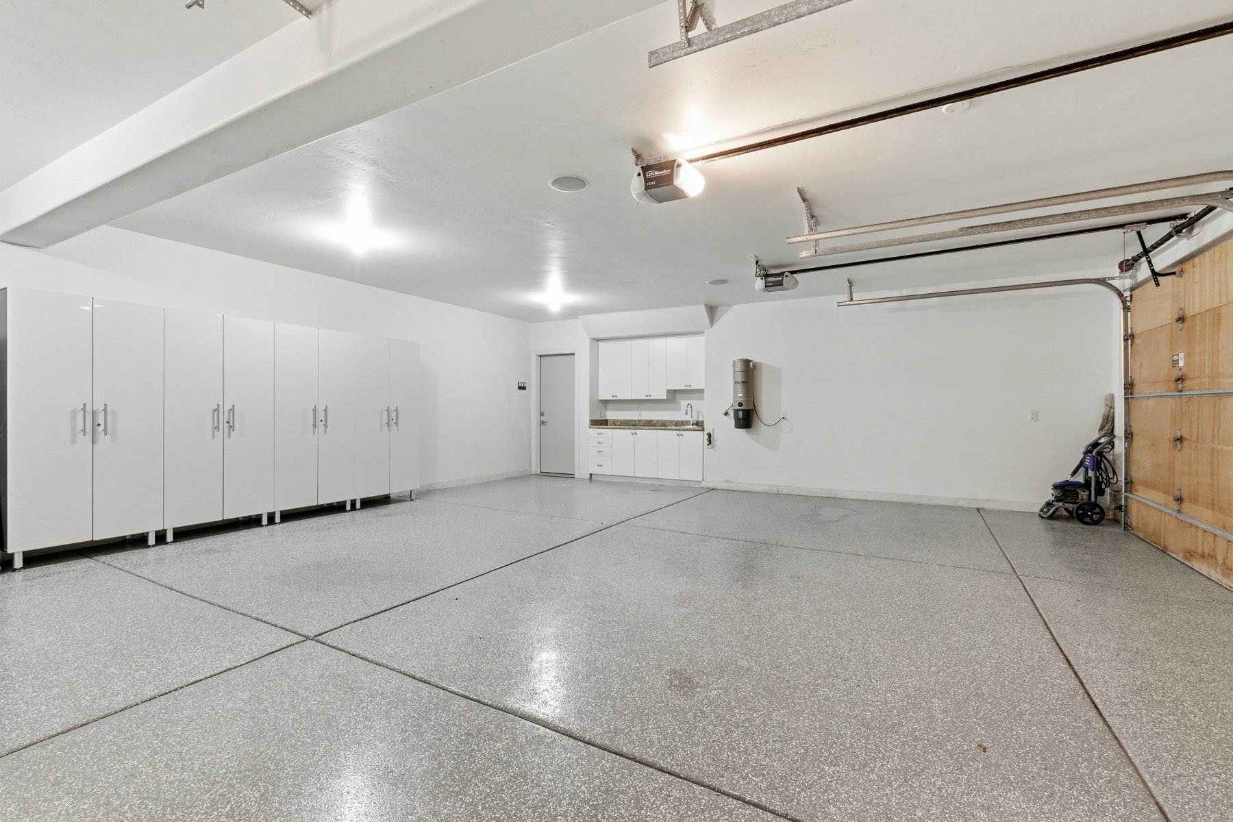 Spacious garage featuring an epoxy-coated concrete floor, extensive white cabinetry with brushed nickel hardware, recessed lighting, and a utility sink area with additional storage