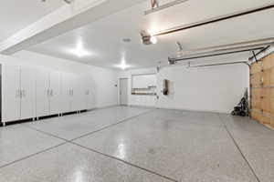 Spacious garage featuring an epoxy-coated concrete floor, extensive white cabinetry with brushed nickel hardware, recessed lighting, and a utility sink area with additional storage