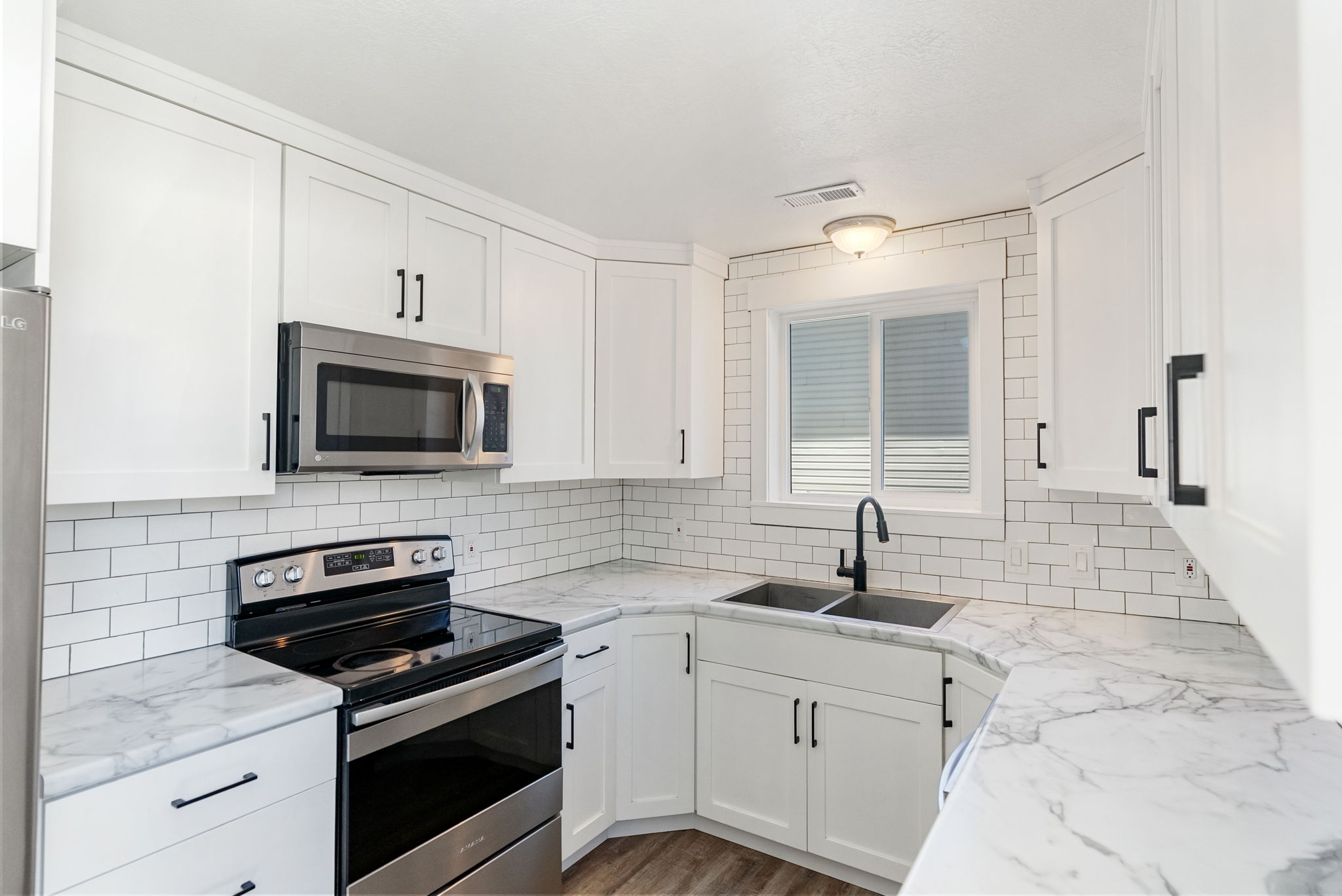 Modern kitchen featuring white shaker cabinetry, stainless steel appliances, marble-look countertops, subway tile backsplash, and wood-finish flooring