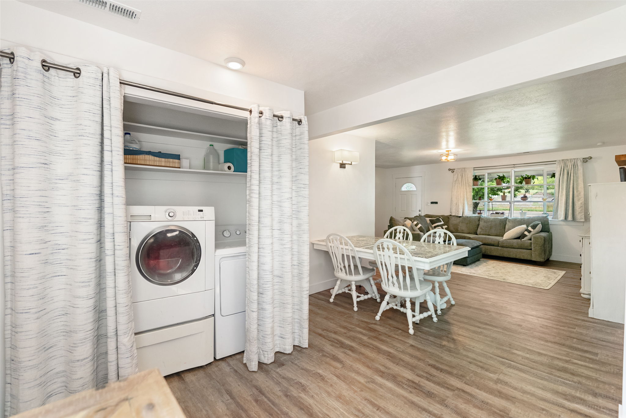 Dedicated laundry closet featuring a stackable washer and dryer, adjacent to a dining area with wood-finish flooring