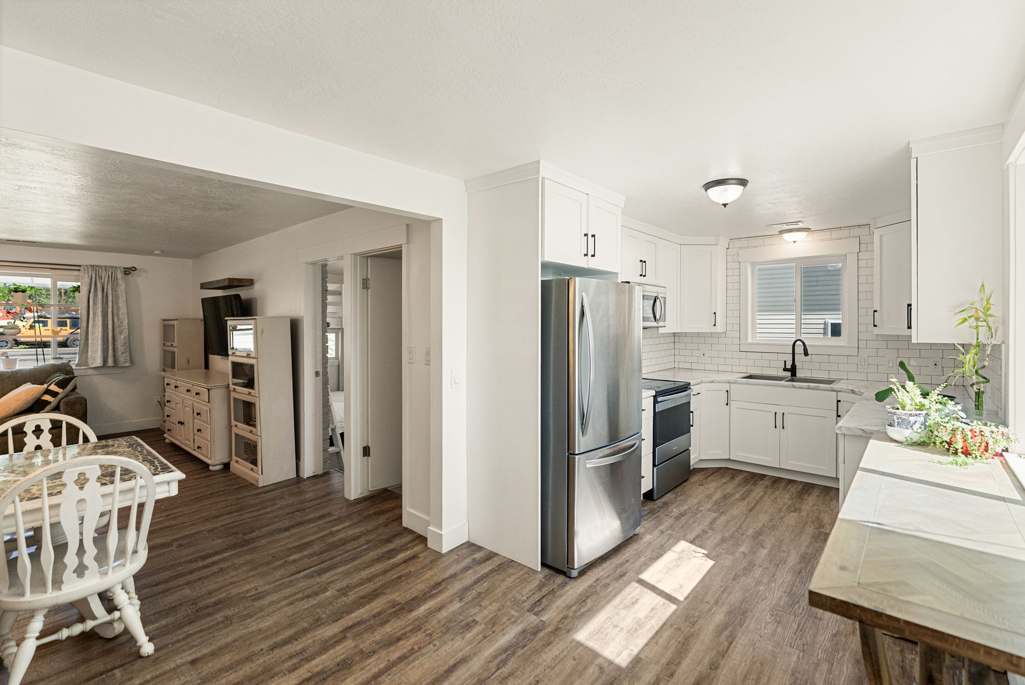 Modern kitchen featuring white shaker cabinetry, stainless steel appliances, a white subway tile backsplash, and wood-finish flooring