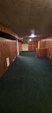 Spacious lower-level room featuring rich wood paneling, dark green carpeting, and a built-in bar