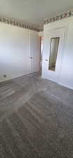 Wall-to-wall carpeting with a light gray hue, white painted walls, and a floral-patterned wallpaper border
