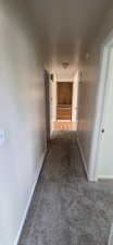 Hallway with carpet flooring, light neutral wall paint, and white trim