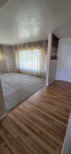 Wood-finish flooring entry leading to a carpeted living space with a large window featuring full-length drapes